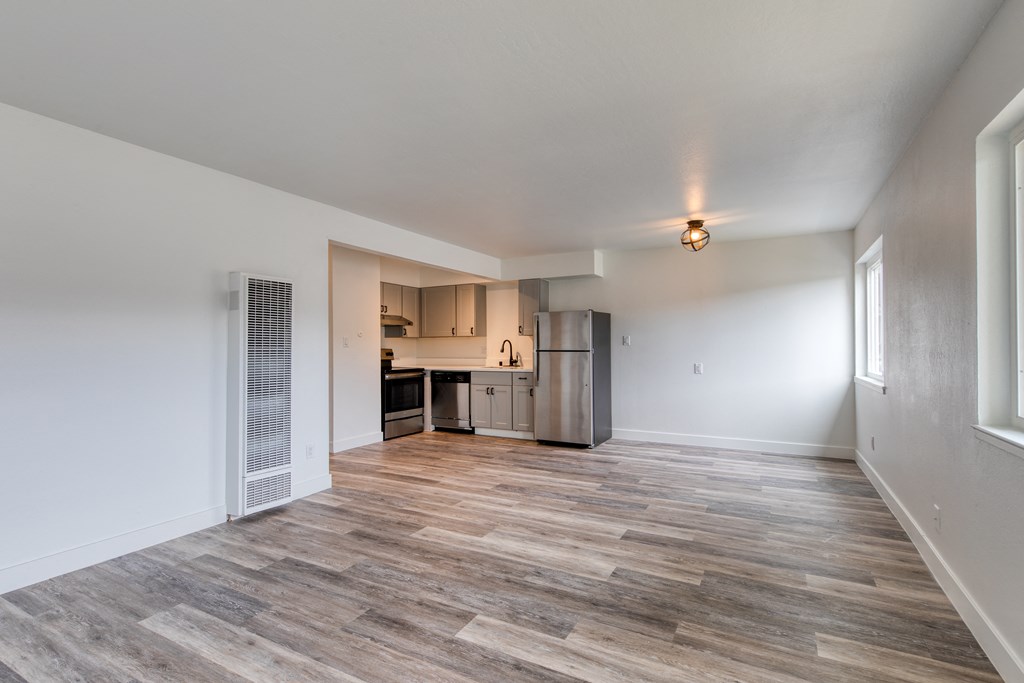 an empty living room with a kitchen in the background