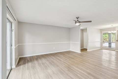A room with a ceiling fan and light, hardwood floors, and a door leading to another room.