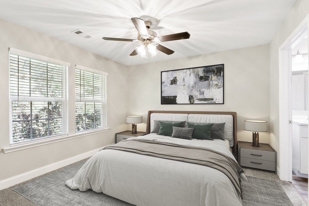 a bedroom with a ceiling fan and two windows