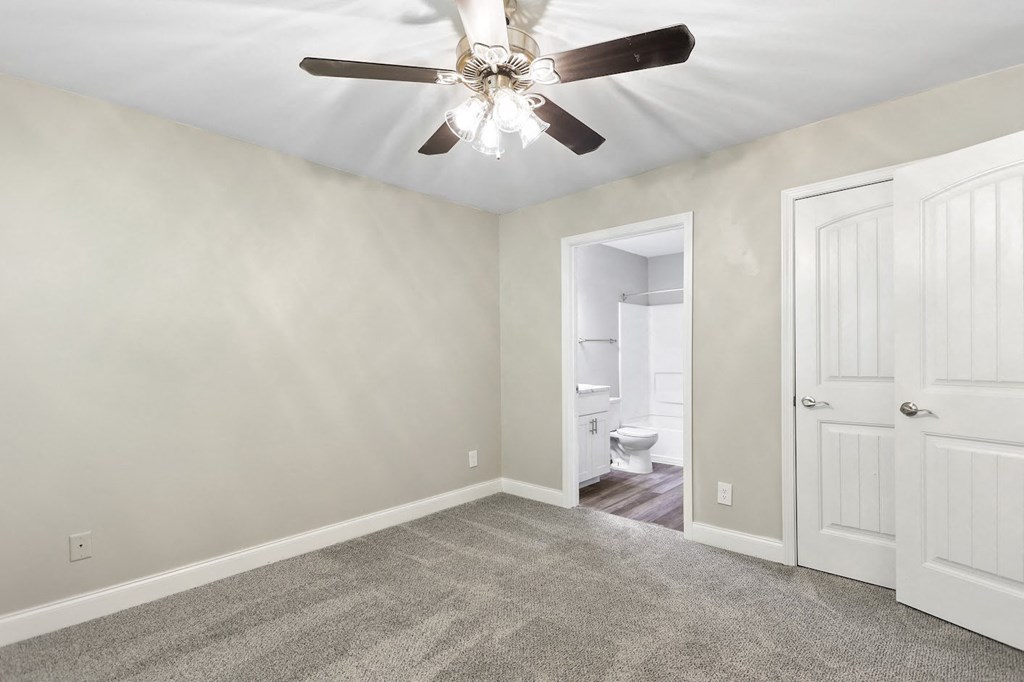 a bedroom with a ceiling fan and a door to a bathroom