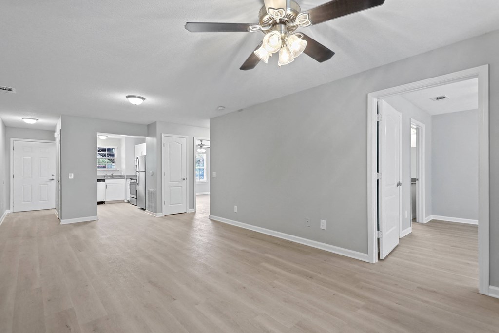 an empty living room with a ceiling fan and a kitchen