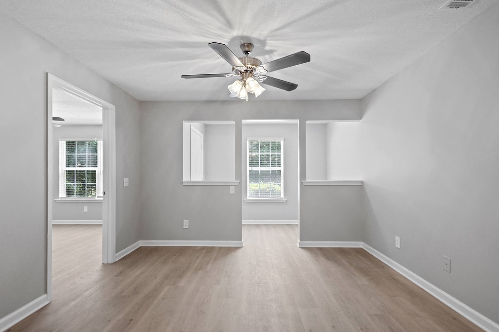 an empty living room with a ceiling fan and windows