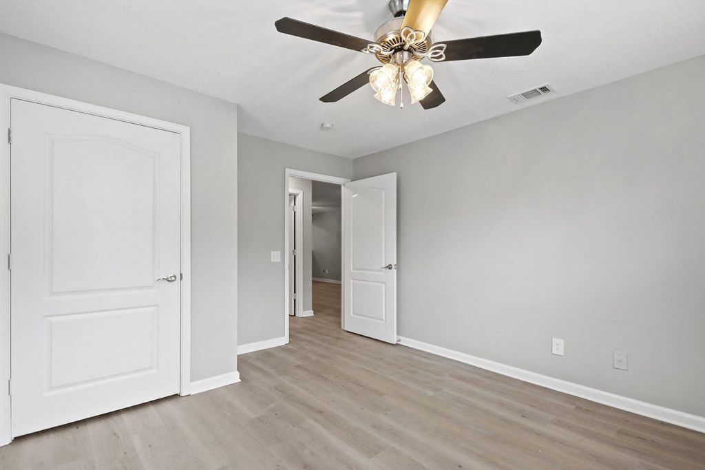 an empty living room with a ceiling fan and a door to a hallway