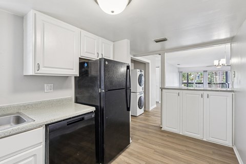 A black refrigerator is in a kitchen with white cabinets.