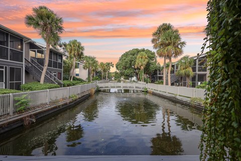 A canal with buildings on either side and a sunset in the background.