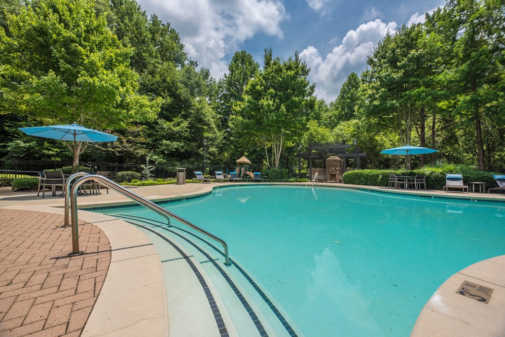 a swimming pool with trees in the background and blue umbrellas