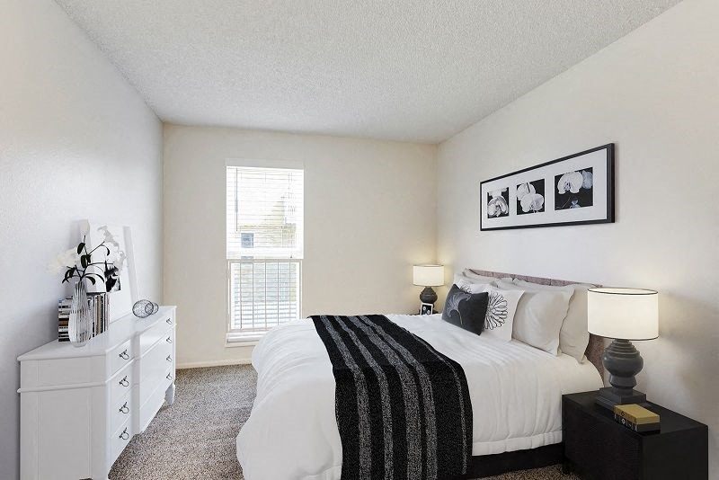 A bedroom with a large bed, nightstand, and a window with blinds.