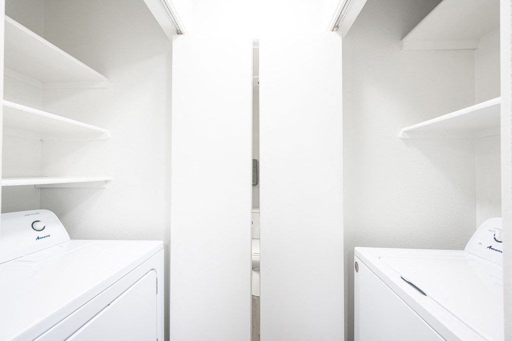 a washer and dryer in a laundry room with white walls and white shelves