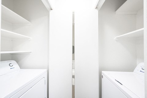 a washer and dryer in a laundry room with white walls and white shelves