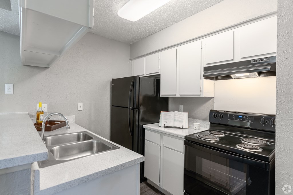 A kitchen with a black refrigerator, white cabinets, and a stove top oven.
