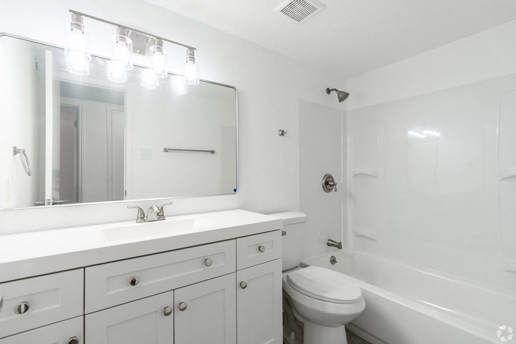 A white bathroom with a sink, mirror, toilet and bathtub.