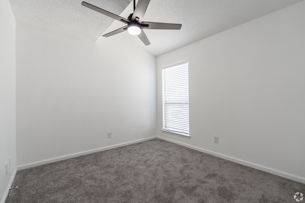 A room with a ceiling fan and a window with blinds.