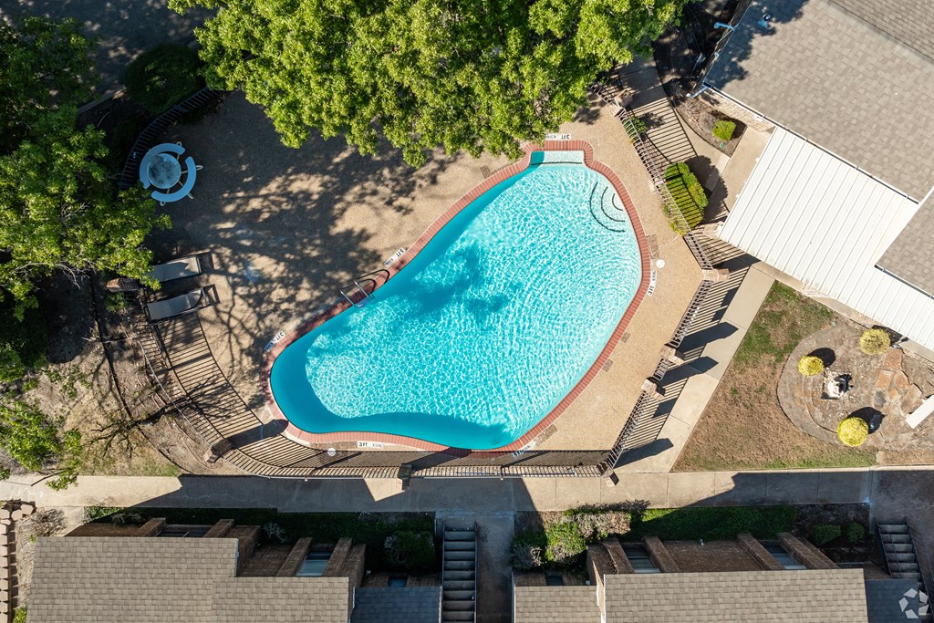 An aerial view of a swimming pool surrounded by trees and buildings.