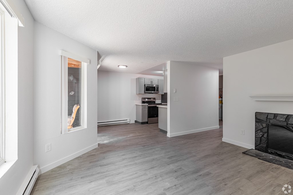A living room with a fireplace and a kitchen in the background.