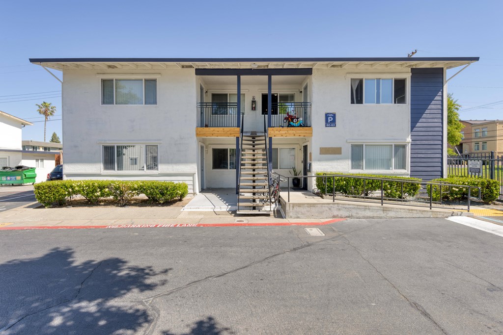a white apartment building with a staircase and a parking lot in front of it