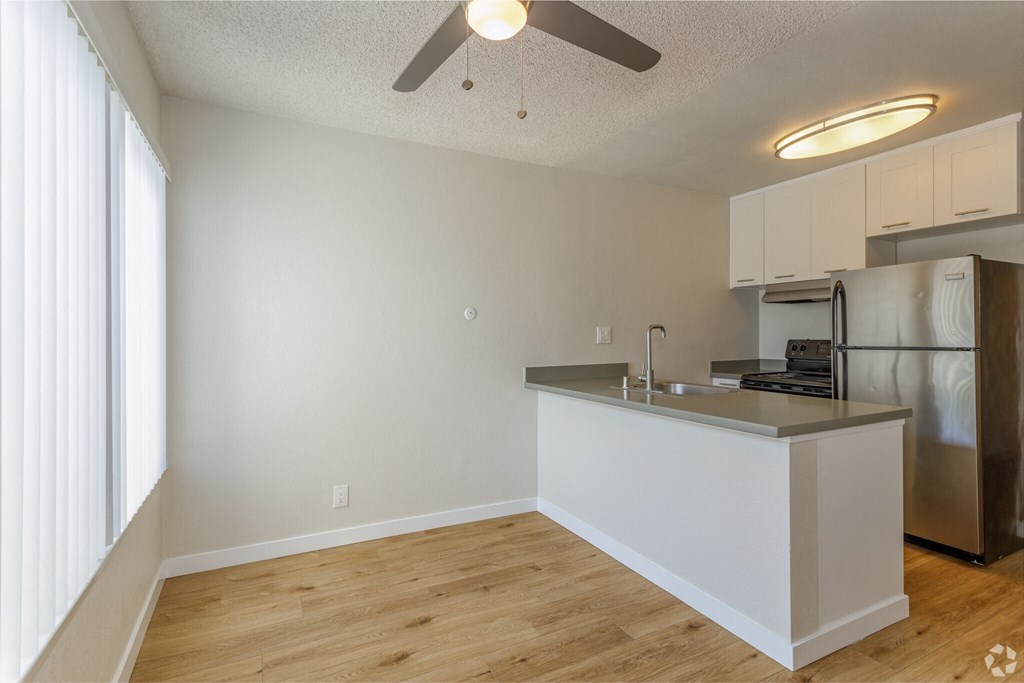 an empty living room with a kitchen and a ceiling fan