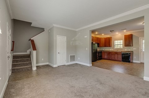an empty living room with a kitchen and a staircase