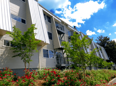A building with a grey facade and red flowers in front.