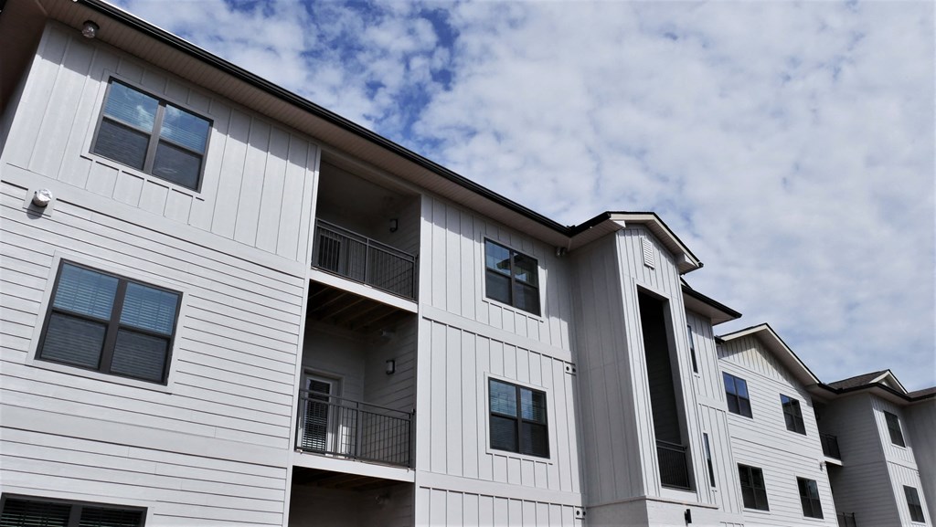 the exterior of a multifamily building with a cloudy sky in the background