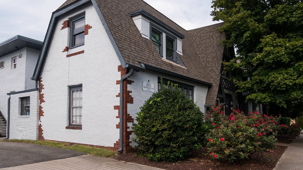the side of a white house with bushes and a tree