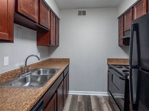 A kitchen with a black refrigerator and brown cabinets.