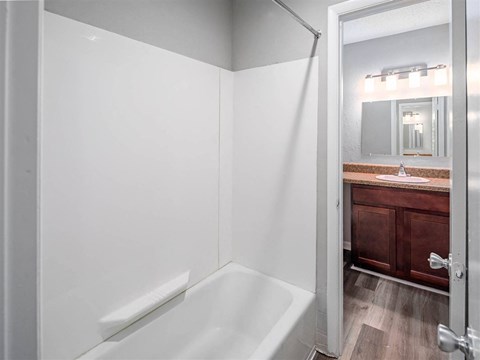A white bathroom with a wooden vanity and a white bathtub.