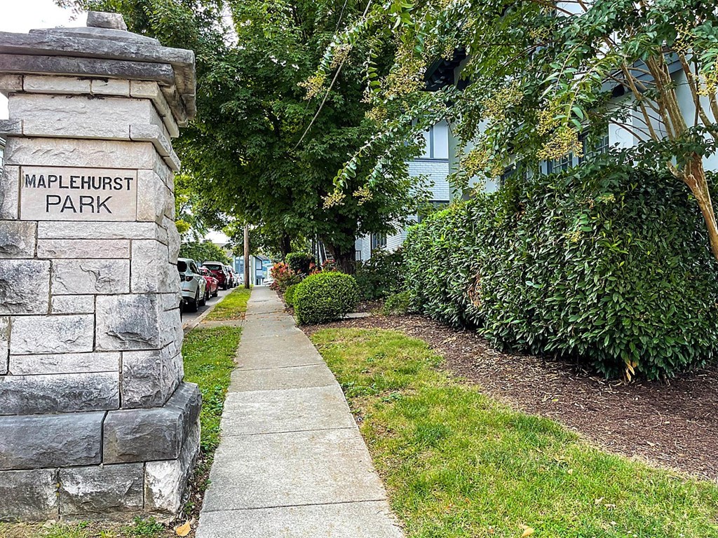 a sidewalk in front of a park next to a stone wall