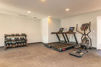 A room with a treadmill, a stationary bike, and a bench with dumbbells.