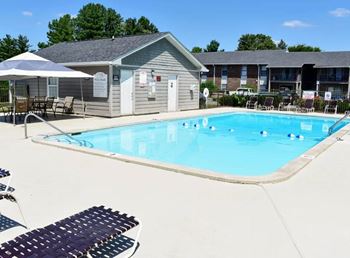 A pool with a sun lounger and umbrella in front of a building.
