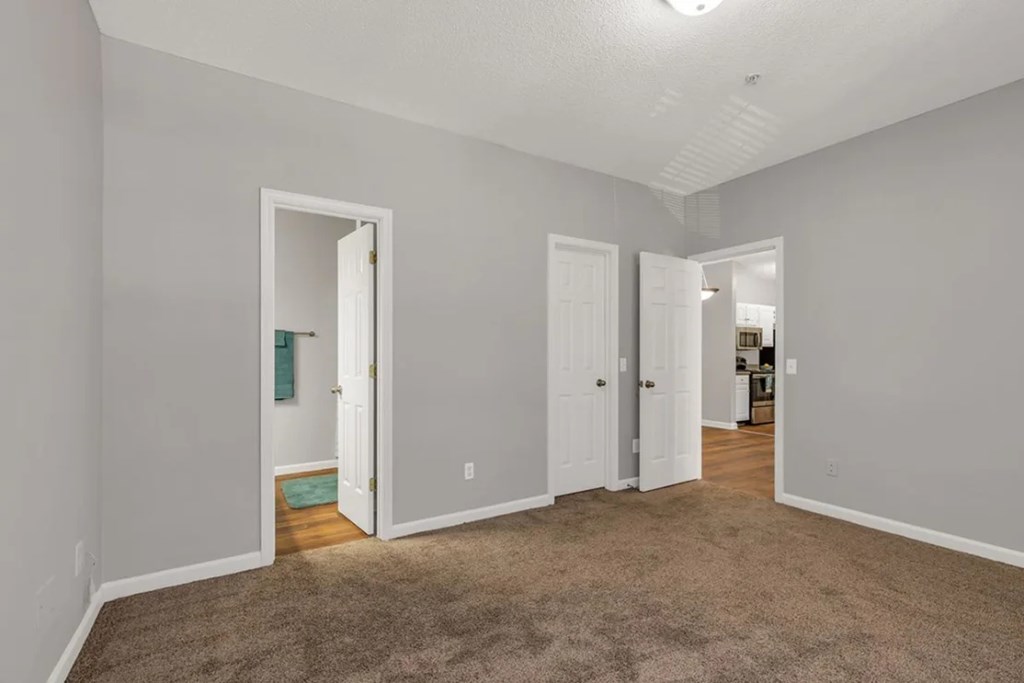 A room with carpeted floor and white walls with two doors.