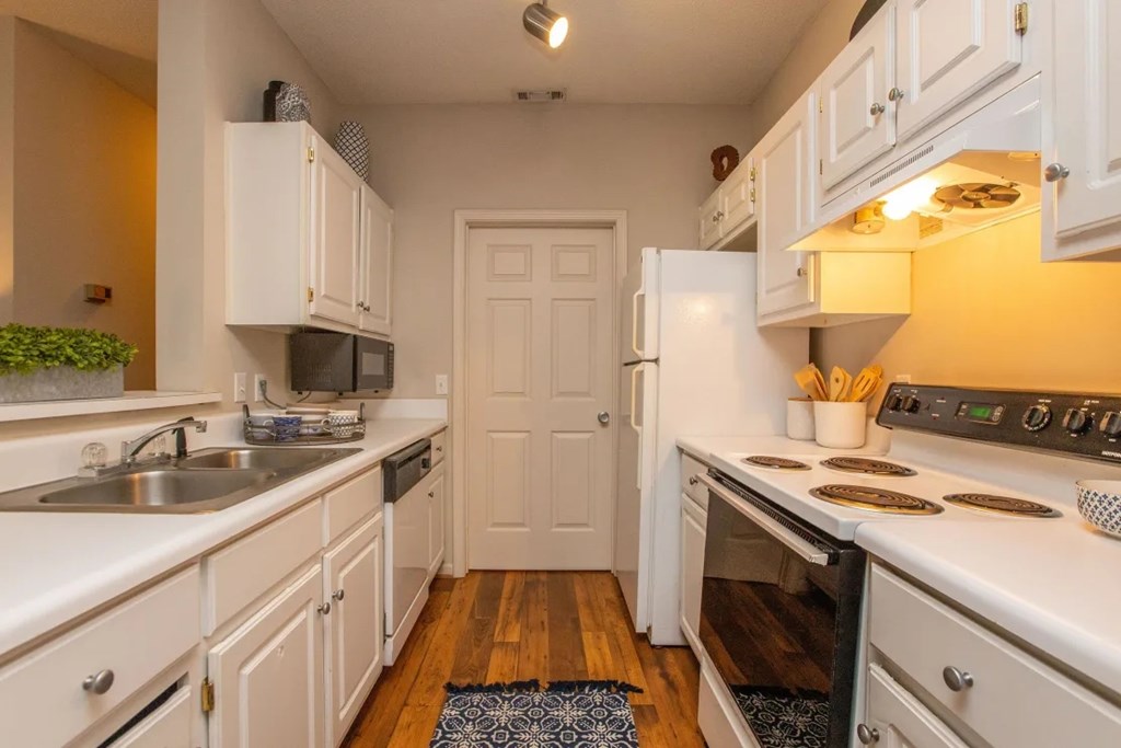 A kitchen with white cabinets and appliances, a sink, and a door in the background.
