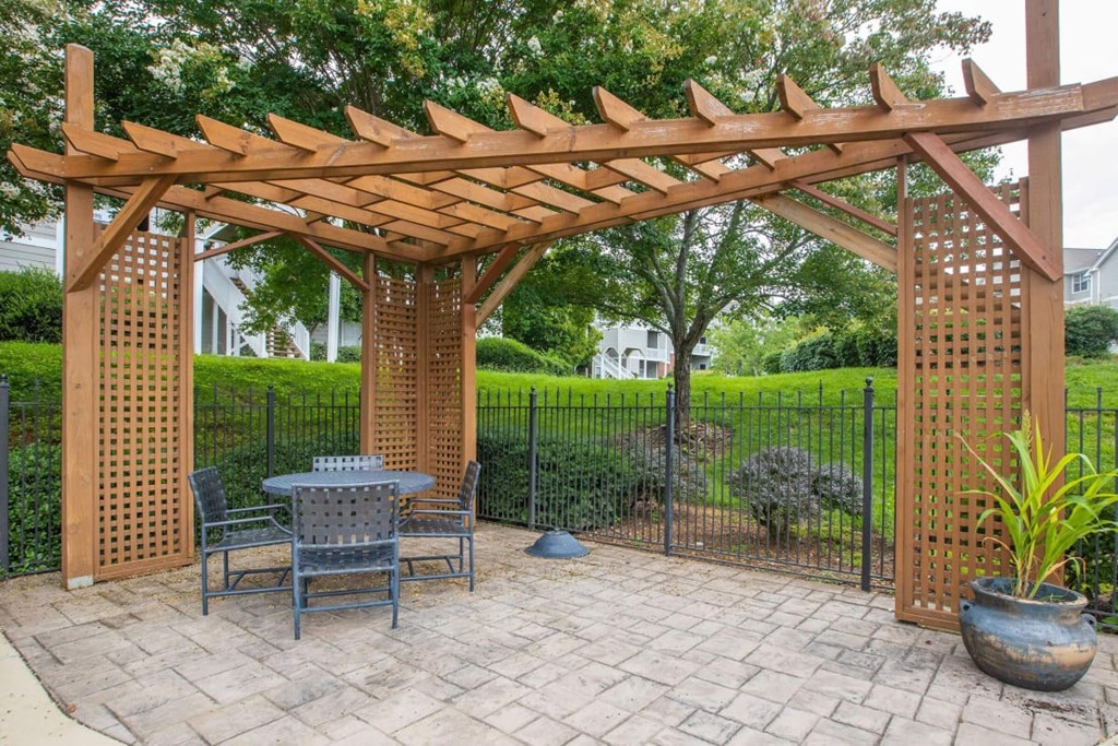 A wooden pergola with a table and chairs underneath it.