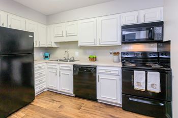 A black refrigerator is on the left in a kitchen with white cabinets.
