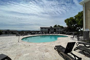 A pool surrounded by a patio and chairs.