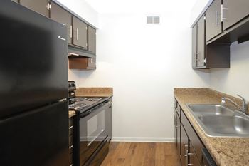 A kitchen with a black fridge, stove and a sink.