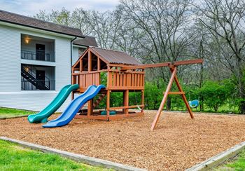 A wooden swing set with a green and blue slide in front of a white house.