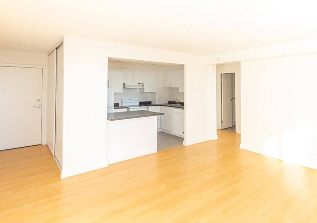 an empty living room with a kitchen in the background