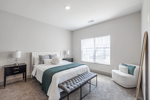 A bedroom with a bed, chair, and nightstand.