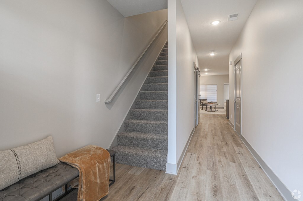 A long hallway with a staircase and a bench with a blanket on it.