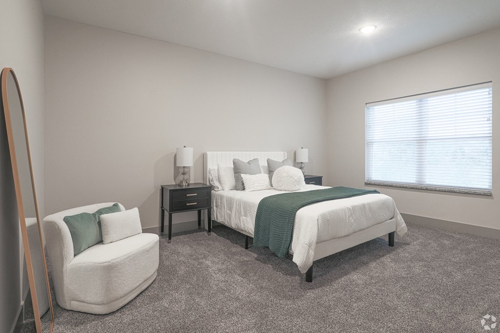 A bedroom with a bed, chair, and nightstand.