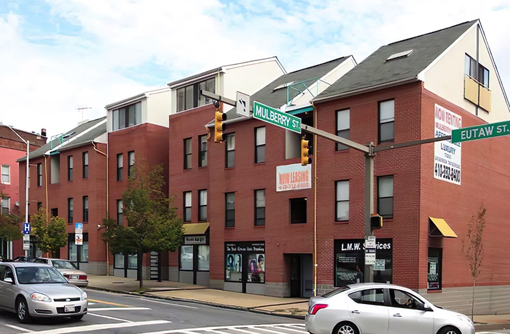 a view of a street corner with a few buildings in the background and cars in the foreground