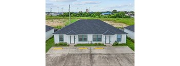 A white house with a black roof is surrounded by a concrete driveway.