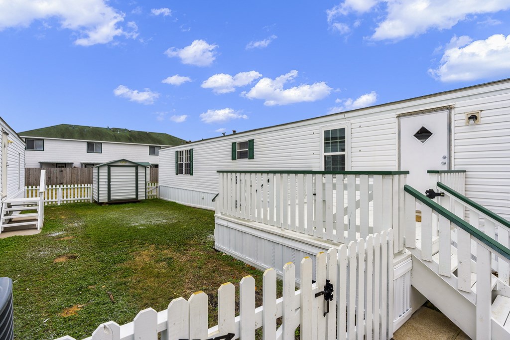 the backyard of a white mobile home with a white fence
