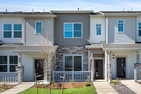 A grey and white townhouse with a front yard and a small tree.