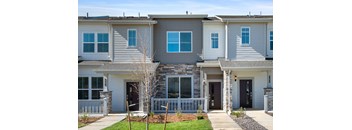 A grey and white townhouse with a front yard and a small tree.