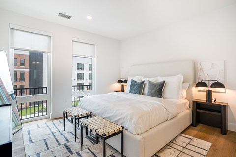 A bedroom with a large bed and a balcony with a view of a building.