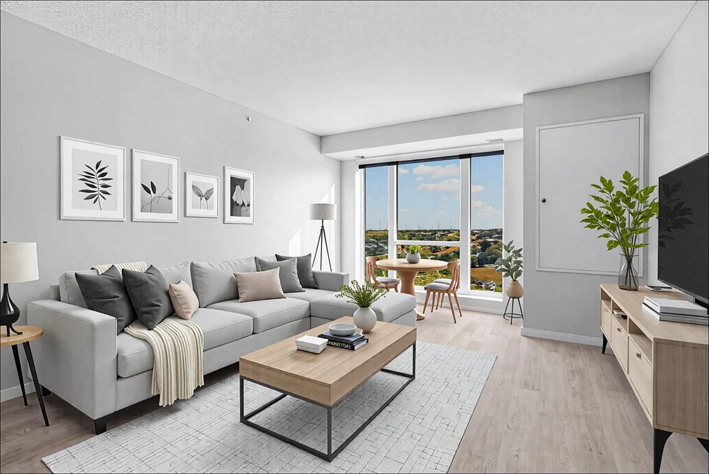 A living room with a grey couch, a coffee table, and a large window with a view of the outdoors.