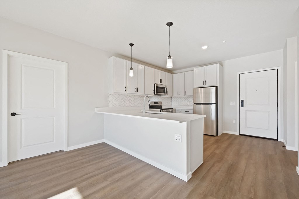 a white kitchen with a large island and a stainless steel refrigerator