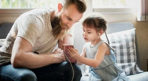 a man and a child sitting on a couch looking at a cell phone