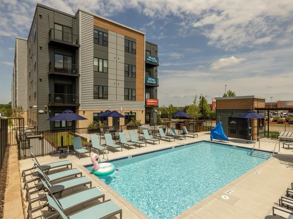 a swimming pool with chaise lounge chairs and umbrellas in front of a building